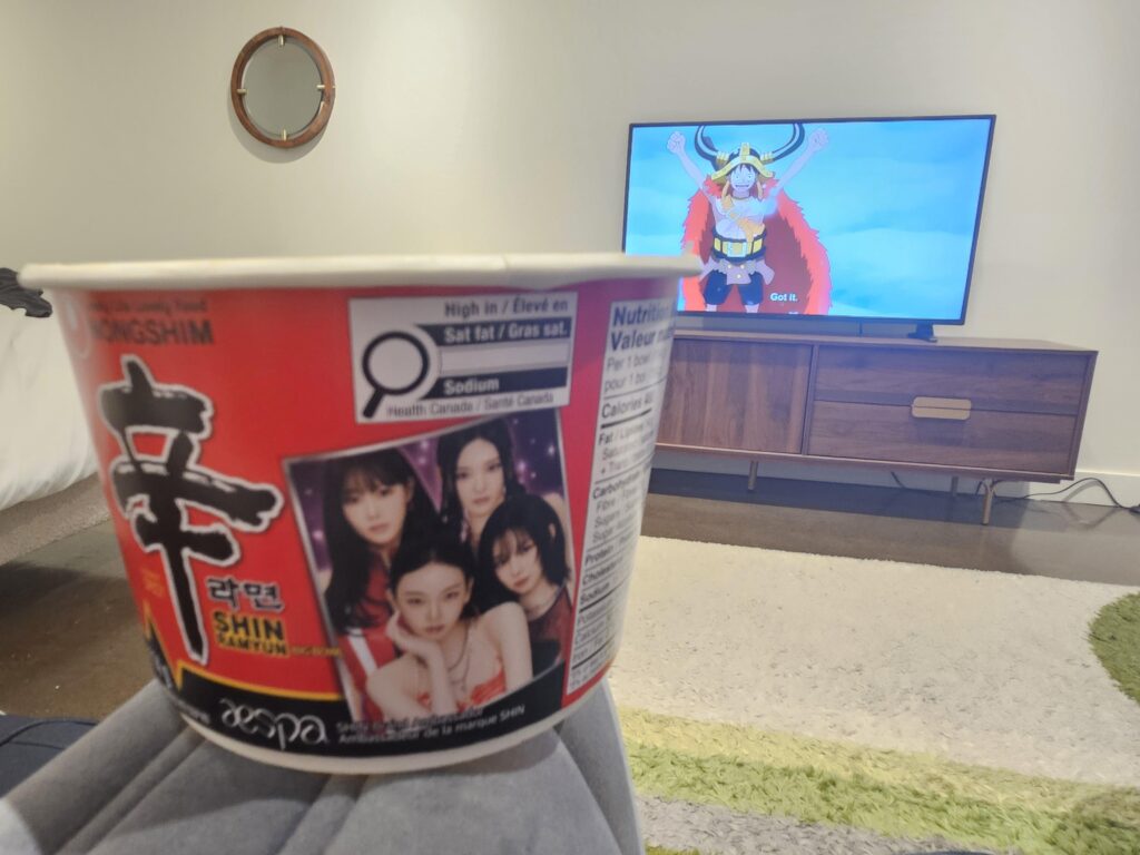 Enjoying an aespa Shin Ramyun bowl in my hotel room while watching One Piece